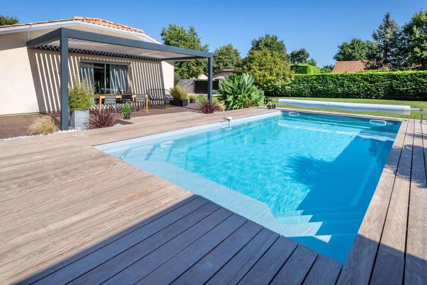 Bassin Maeva 8 bordé d’une terrasse en bois, devant une pergola.